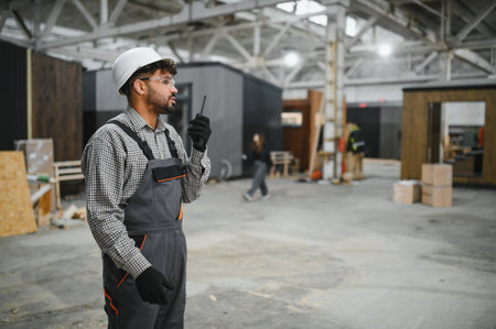 Arab construction worker wearing safety helmet and using walkie talkie in a prefabricated house factoryの写真素材