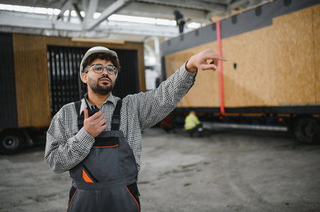 Construction worker using walkie talkie and pointing while supervising modular house transport in a...