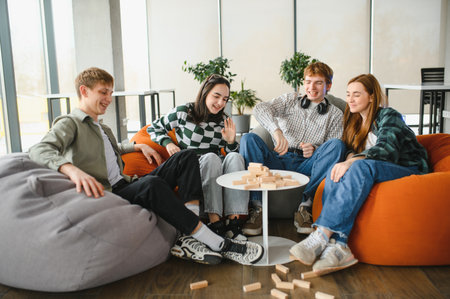 Four university students enjoying their free time playing jenga, sitting on beanbag chairs in a...