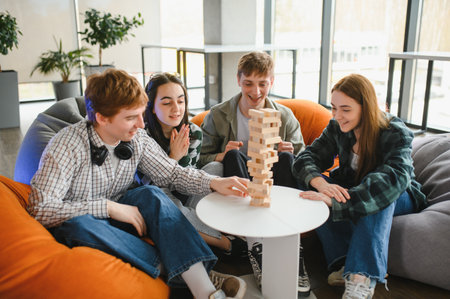 Four happy friends enjoying their free time by playing a stacking tower wood block game in a modern...
