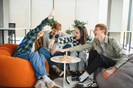 Four cheerful young adults enjoying their free time playing a strategy board game, laughing and...