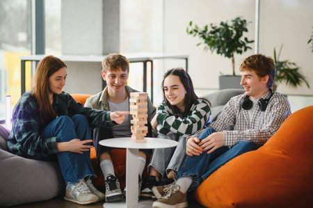 Group of young adults enjoying a lively stacking game in a modern coworking space, laughing and...