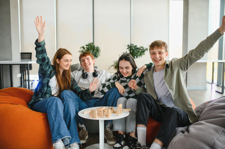 Four cheerful college students are enjoying a lively board game in the university lounge, celebrating their victory with enthusiastic high fives and joyful laughterの写真素材
