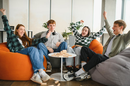 Four teenagers are sitting on beanbag chairs, playing a game with wooden blocks, having fun and enjoying their time togetherの写真素材