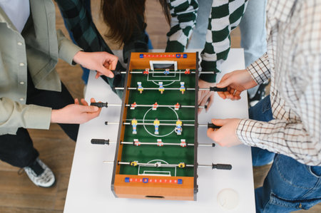 Cheerful young startup employees are playing table football, having fun together during a break in...