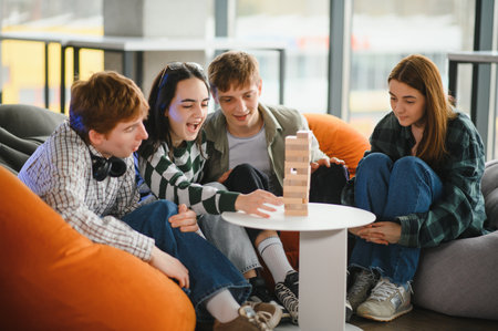 Four young friends are sitting on beanbag chairs, enjoying a friendly board game, carefully removing...