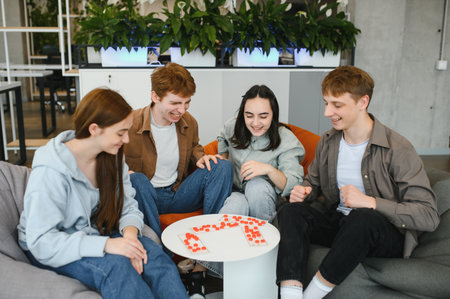 Four cheerful colleagues enjoying a board game during break time in a modern office space, fostering teamwork and camaraderieの写真素材