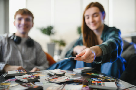 Two friends enjoying a lively card game at home, smiling and laughing while holding colorful cards,...