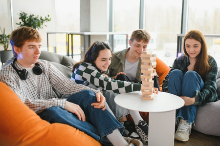 Four young friends are sitting on comfortable beanbag chairs in a modern living room, enjoying a...