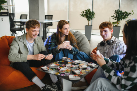 Four young colleagues are sitting on beanbag chairs in a modern office, playing cards and having fun...