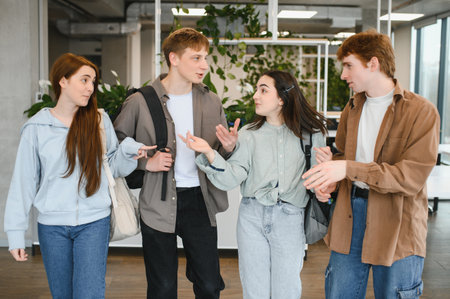 Four college students walk together through the university hallway, talking and gesturing as they...