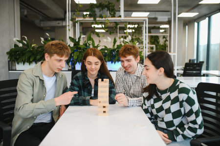 Four young colleagues enjoying a game of wooden blocks, enhancing teamwork and communication skills...