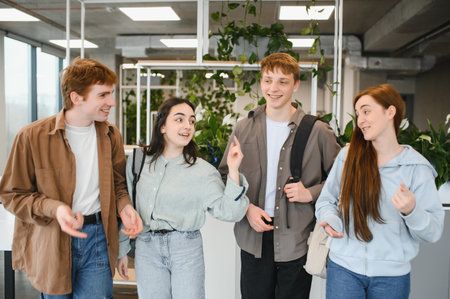 Four cheerful students are enjoying their time together, walking and chatting in a modern university hallway, adorned with lush green plantsの写真素材