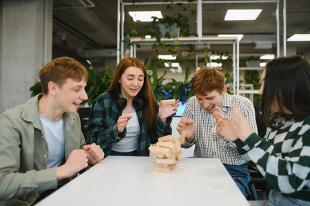 Four young startup employees are having fun in the office break room playing a wood block game