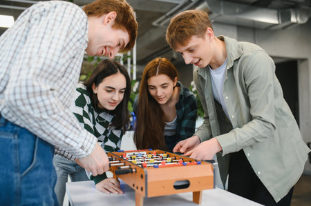 Four cheerful young startup business colleagues having fun together playing table football in the...