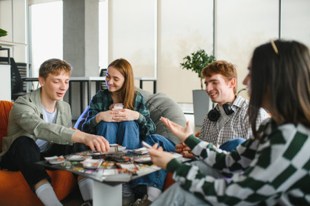Four college students laughing and enjoying their free time while playing cards in a vibrant...