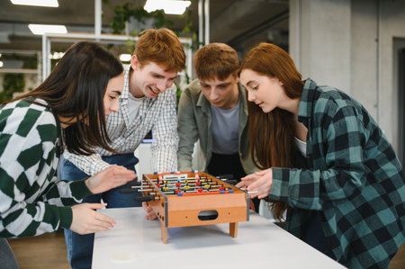 Four cheerful young startup colleagues enjoying a lively break, engaging in a friendly game of table...