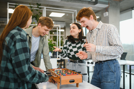 Cheerful young startup coworkers playing table football, having fun together during a break in a modern officeの写真素材