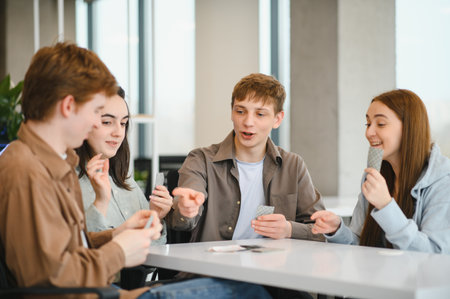 Four cheerful university students are sitting around a table in a break room, enjoying a friendly...