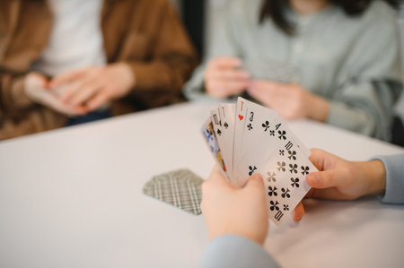 Friends gathered around a table, playing cards and enjoying laughter during their leisure time,...