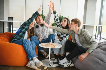 Four cheerful students are giving a high five after playing a board game together at home,...