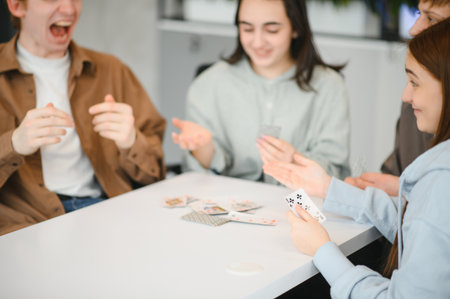 Group of cheerful young adults enjoying their leisure time, playing cards and having fun together...