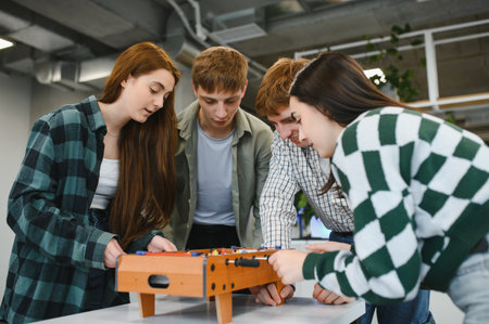 Four young startup colleagues enjoying a friendly game of table football during a break, fostering teamwork and camaraderie in a modern office environmentの写真素材