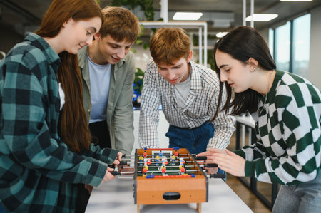 Four cheerful young office workers are enjoying their break time playing table football together