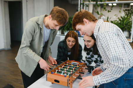 Four cheerful young startup colleagues enjoying a friendly game of table football during a break in...