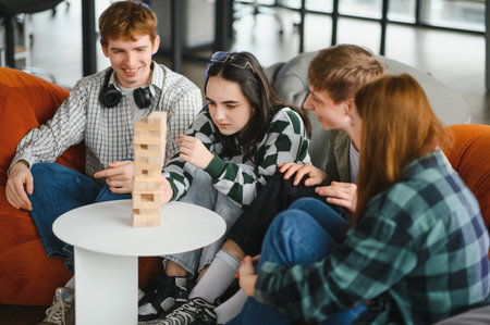 Group of cheerful young friends enjoying their leisure time, playing a captivating board game and...