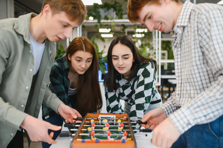 Four cheerful young colleagues are enjoying a friendly game of table football during their break...