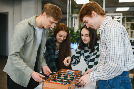 Four young startup colleagues enjoying a friendly game of table football, fostering teamwork and...
