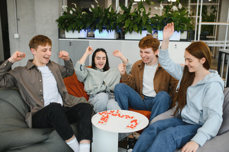 Four cheerful young adults enjoying a board game, raising their arms in excitement after a...