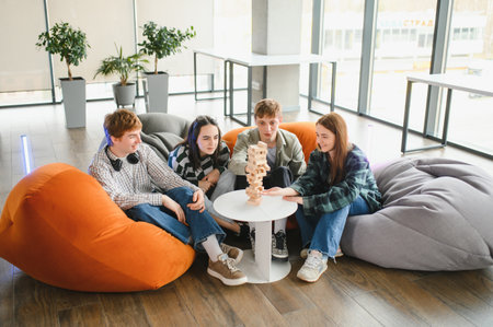 Group of young colleagues enjoying a break, playing a game of wooden blocks in a modern office environment, promoting teamwork and relaxationの写真素材