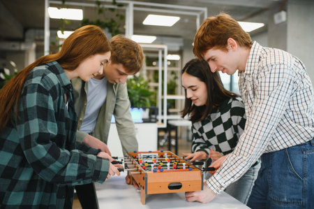 Four young startup employees are enjoying their break time playing table football in the office