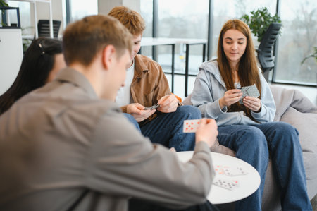 Group of young colleagues enjoying a card game during their office break, fostering camaraderie and...