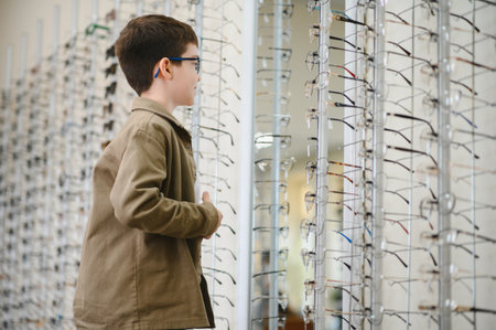 Boy trying on eyeglasses, choosing frames in optics store, ophthalmological vision correction for...