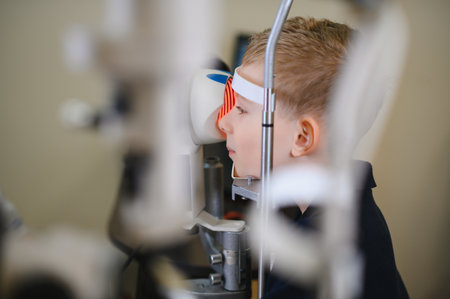 Blond boy having his eyesight checked by an ophthalmologist using a modern medical apparatus in a...