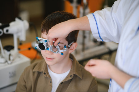 Ophthalmologist examining the eyesight of a young boy with a trial frame during a routine checkup in...