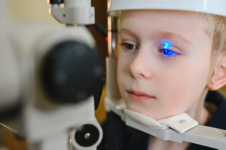 Young boy receiving eye examination with blue laser light in ophthalmology clinic, demonstrating...