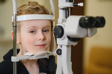 Young boy undergoing an eye examination using a phoropter in an ophthalmology clinic, highlighting...