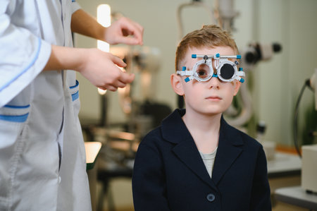 Doctor ophthalmologist examining eyesight of little boy with trial frame checking visual acuity...