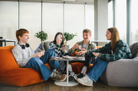 Four cheerful young people playing cards in a modern coworking space, enjoying their leisure time...