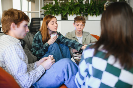 Four friends relaxing on beanbag chairs, enjoying a lively card game, sharing laughter and creating...