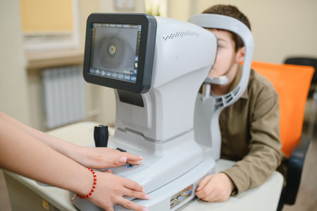 Boy undergoing eye examination with autorefractor by ophthalmologist, checking visual acuity and...