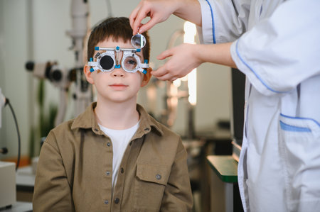 Ophthalmologist examining the eyesight of a young boy with a trial frame during a routine checkup at...