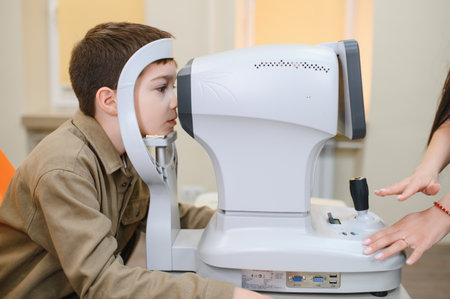 Boy undergoing visual acuity examination using autorefractor in modern ophthalmology clinic,...