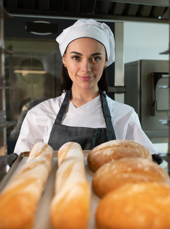 Professional baker presenting a tray filled with an assortment of freshly baked bread and golden...