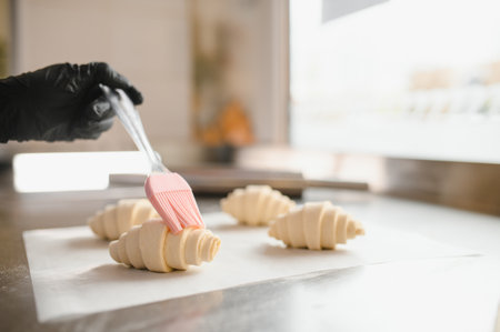 Baker brushing egg wash on raw croissants before baking, adding a golden color and shine to the...