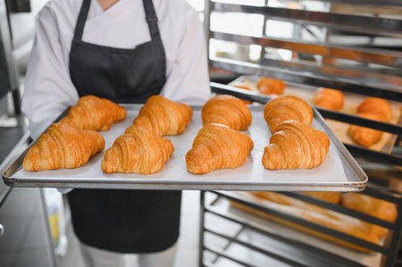 Baker presenting tray of golden brown croissants, showing the result of baking in professional...